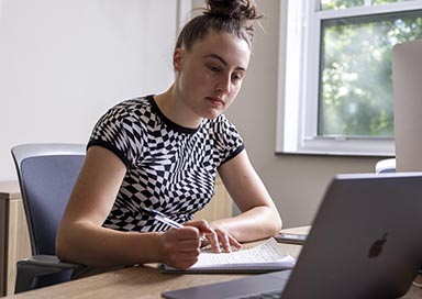 Student writing in front of laptop