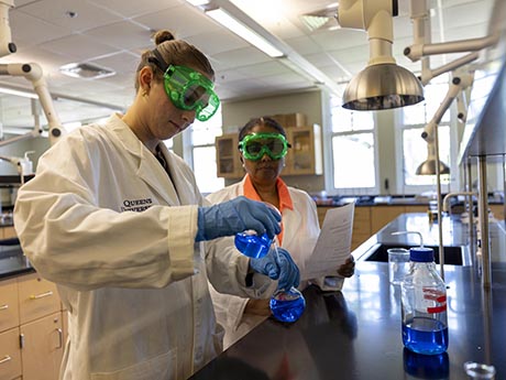 Student measuring blue liquid with professor