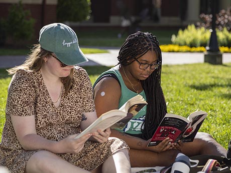 Two students reading books in quad