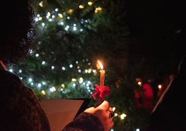 Community member with candle in front of tree