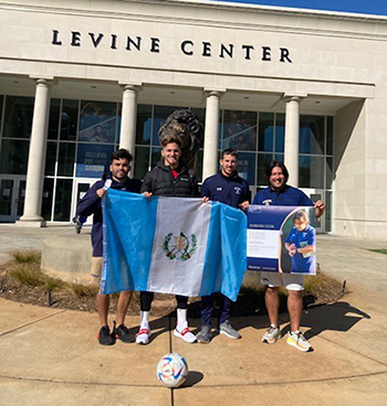 Oliver & soccer players with flag in front of the Levine Center