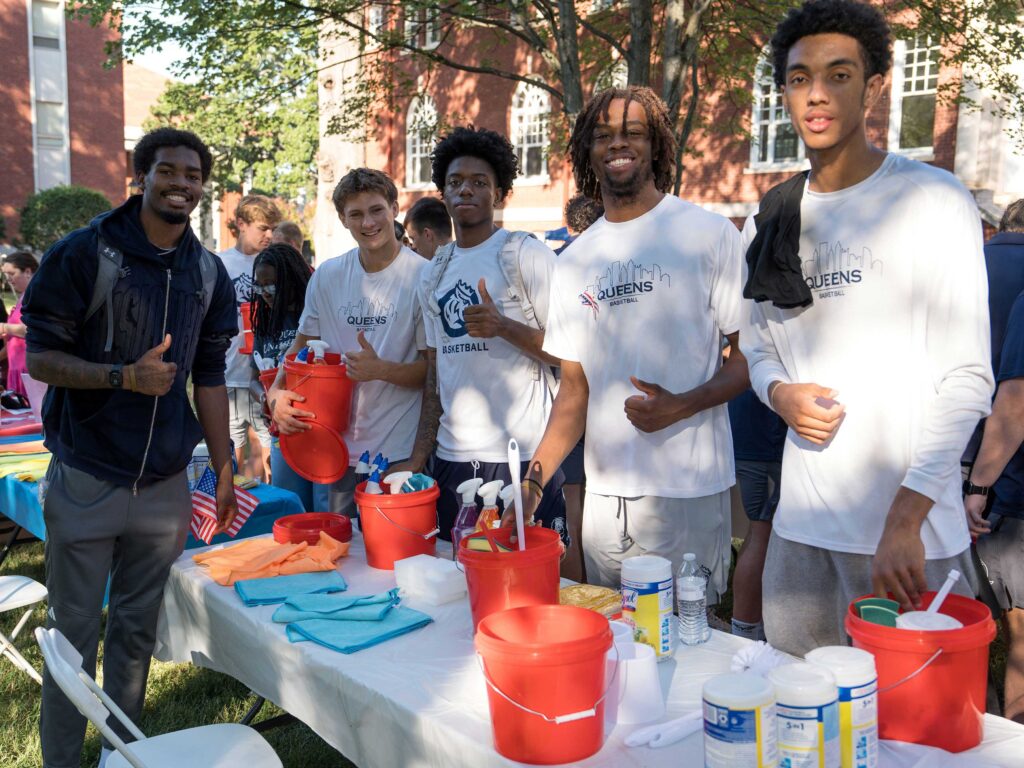 Five students stand aroudn a table assemble small red bucks of cleaning supplies.